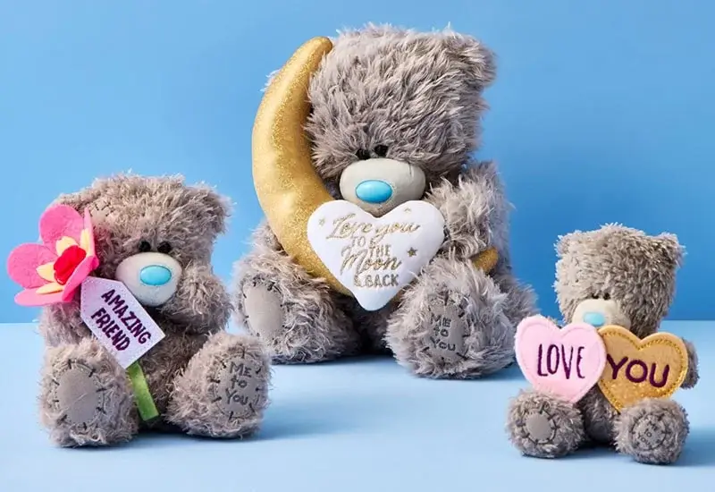 Three grey 'Me to You' teddy bears with blue noses holding heartfelt messages, displayed against a blue background.